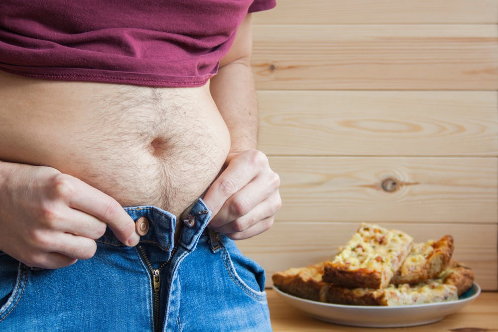 Ein Mann kämpft damit, seine Jeans zuzuknöpfen, weil er übergewichtig ist