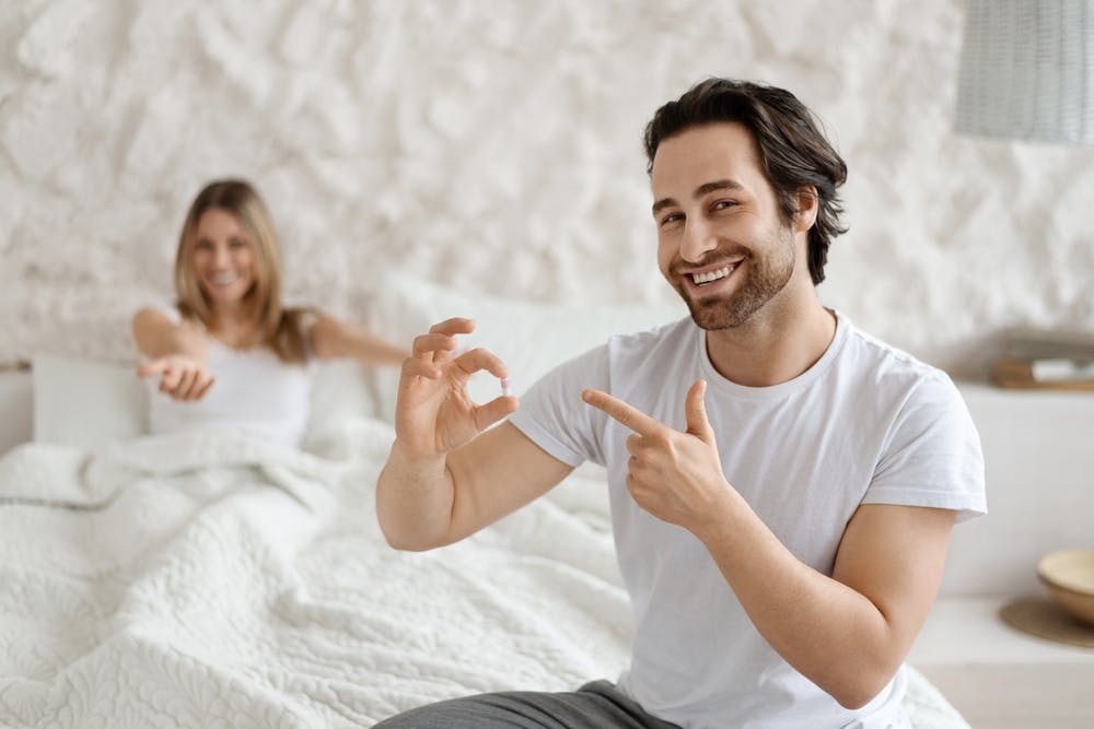 Ein Mann hält eine Viagra-Pille in der Hand und sieht zufrieden aus