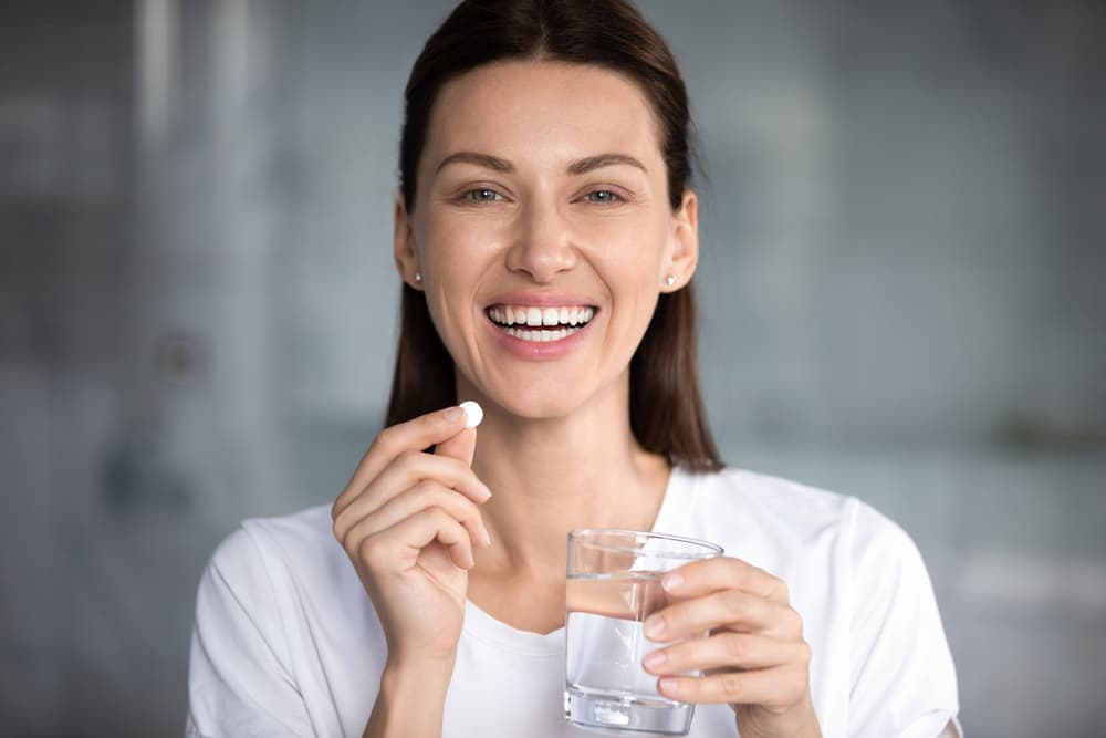 Lächelnde Frau, die eine Yasmin Pille und ein Glas Wasser in der Hand hält