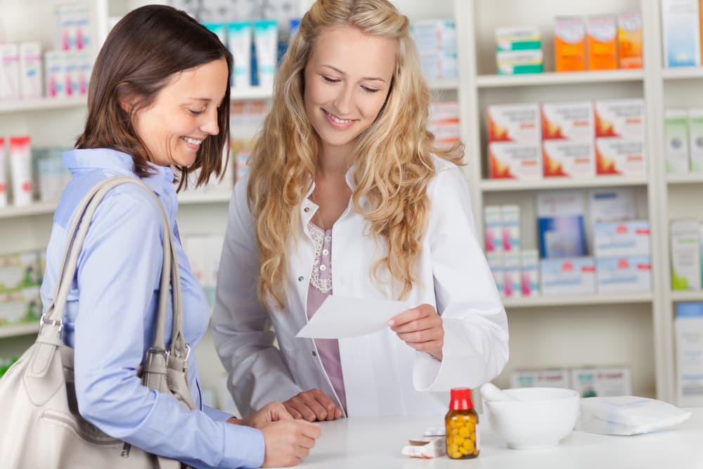 Eine Frau stand in einer Apotheke und sah sich ihr ärztliches Rezept mit einem Apotheker an