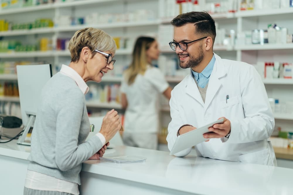 Eine Patientin am Apothekenschalter im Gespräch mit einem Apotheker