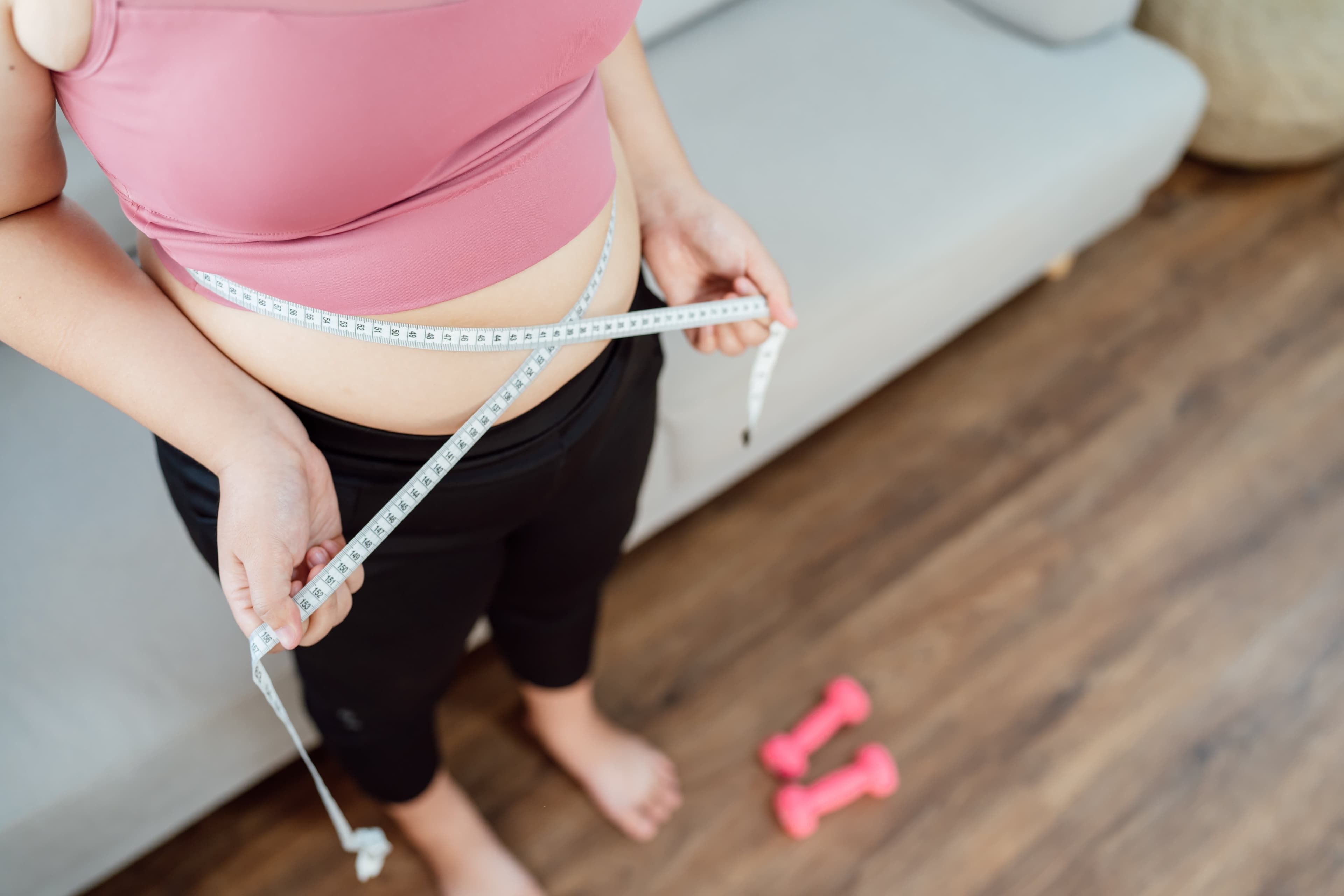 Eine Frau misst ihre Taille mit einem Maßband.