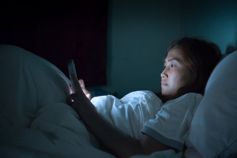 Eine Frau, die im Bett liegt und im Dunkeln mit ihrem Handy spielt