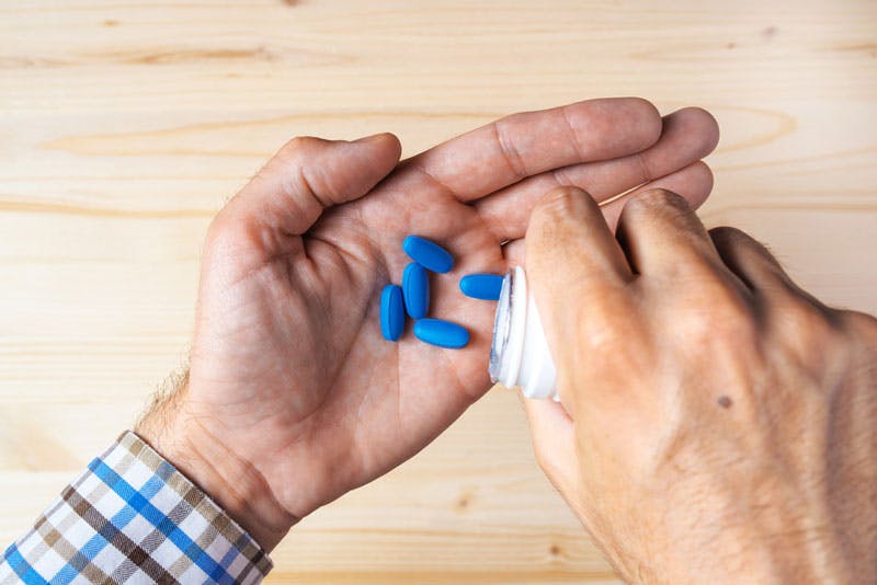 Viagra-Tabletten (die blaue Pille) werden aus der Flasche in eine Hand gegossen