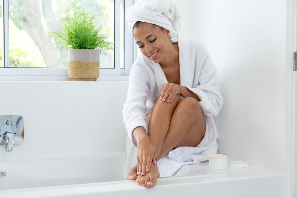 Eine Frau trägt wartec Creme auf ihre Füße auf, während sie in der Badewanne sitzt und sich entspannt
