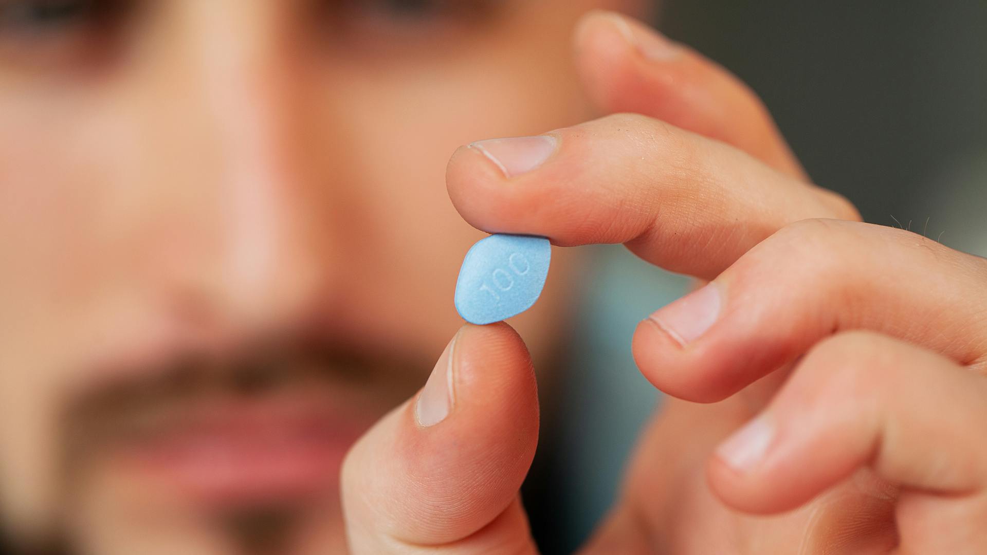 ein Mann, der eine Viagra-Tablette / die blaue Pille hält