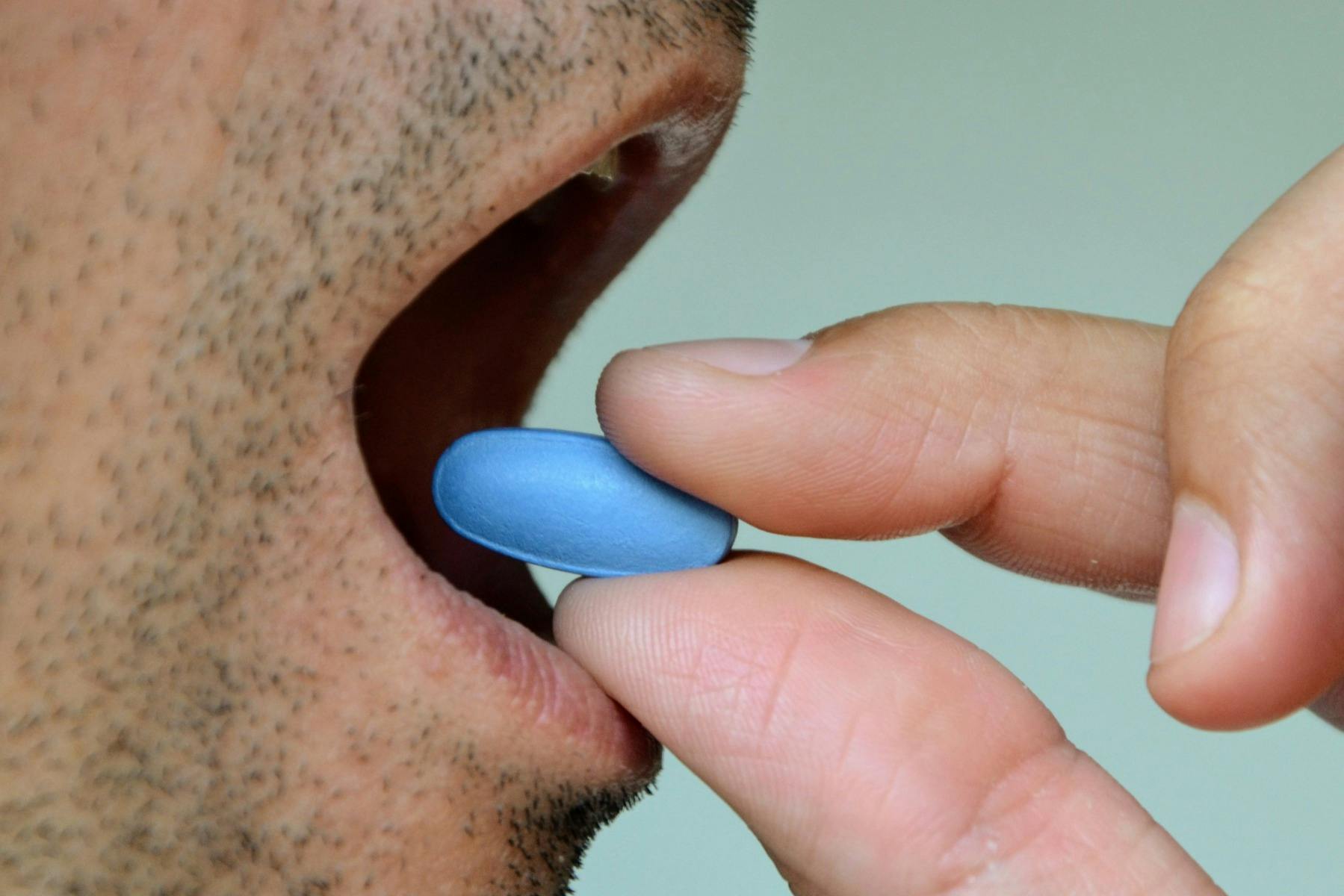 Viagra-Pille (die blaue Pille) wird einem Mann in den Mund gelegt