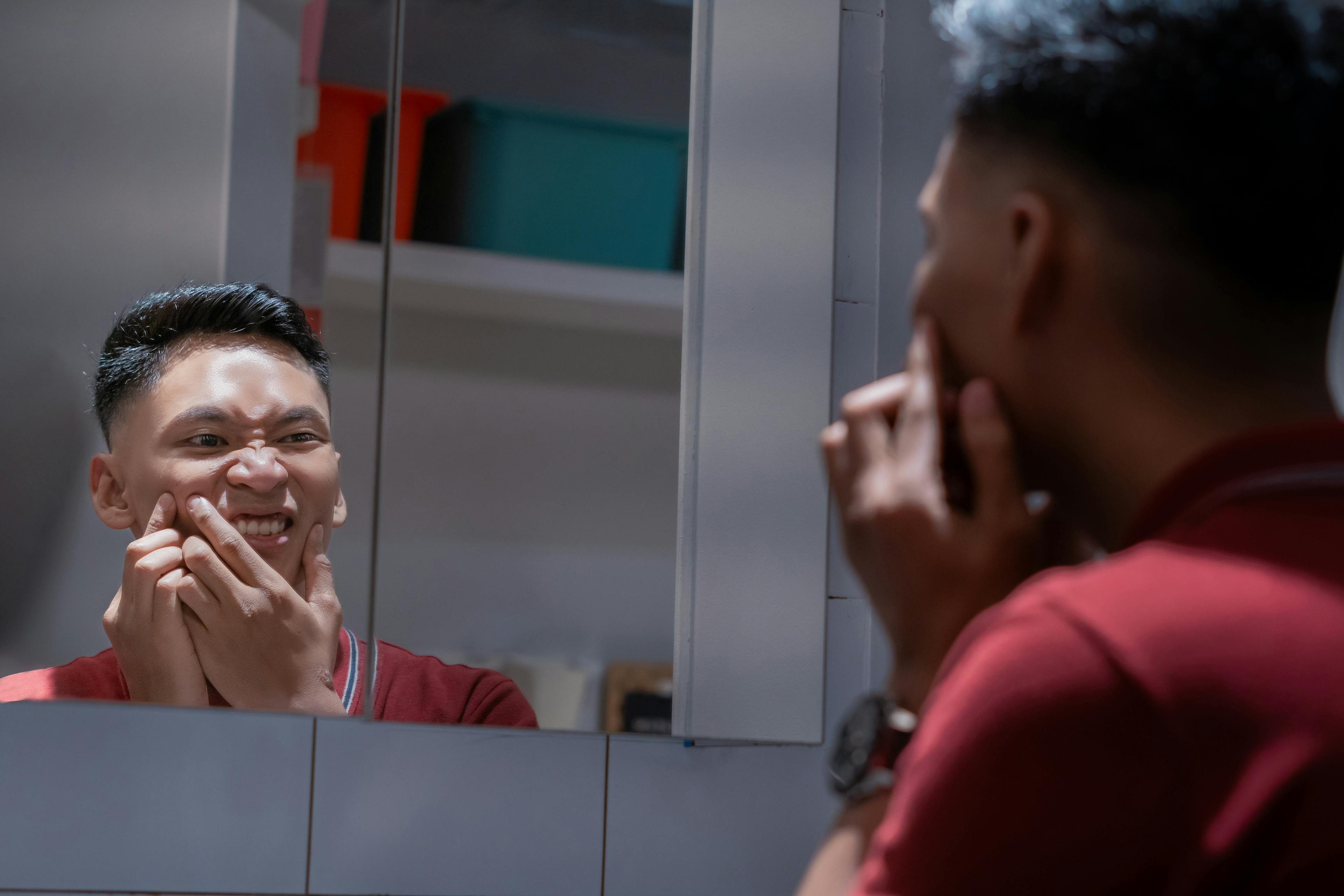 Ein Mann blickt in den Spiegel und sein Gesicht juckt, weil er an Akne leidet