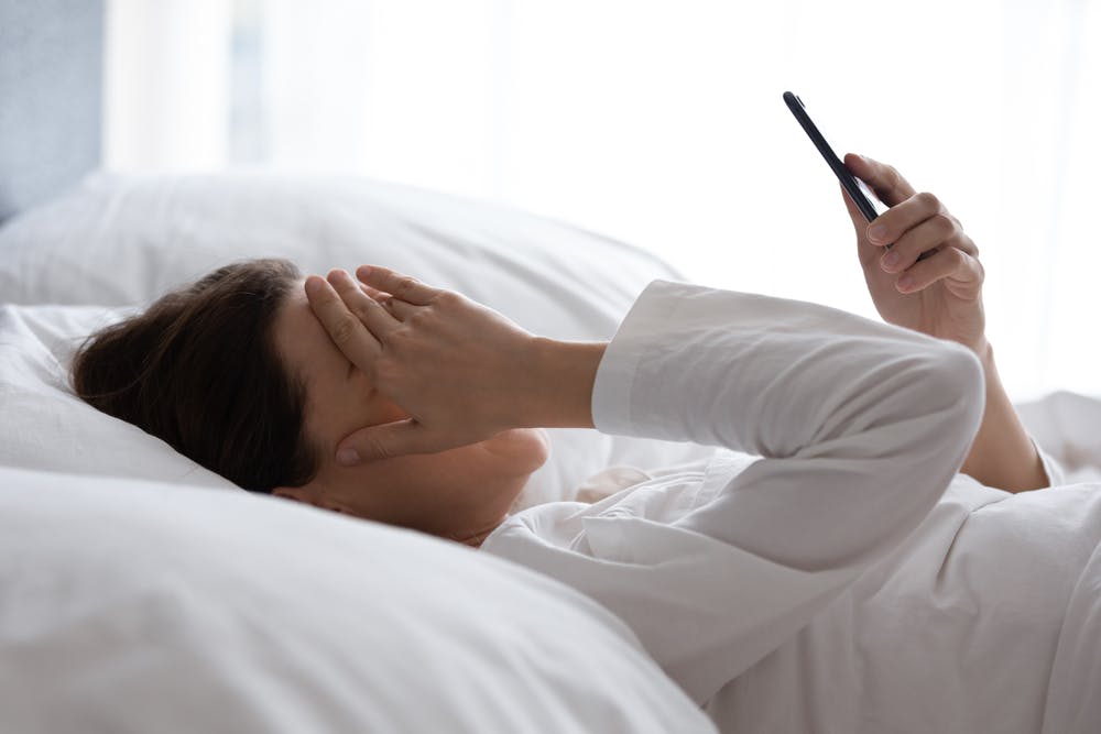 Eine Frau, die auf ihrem Bett liegt und ihren Kopf mit der Hand bedeckt, weil sie an einer Migräne leidet