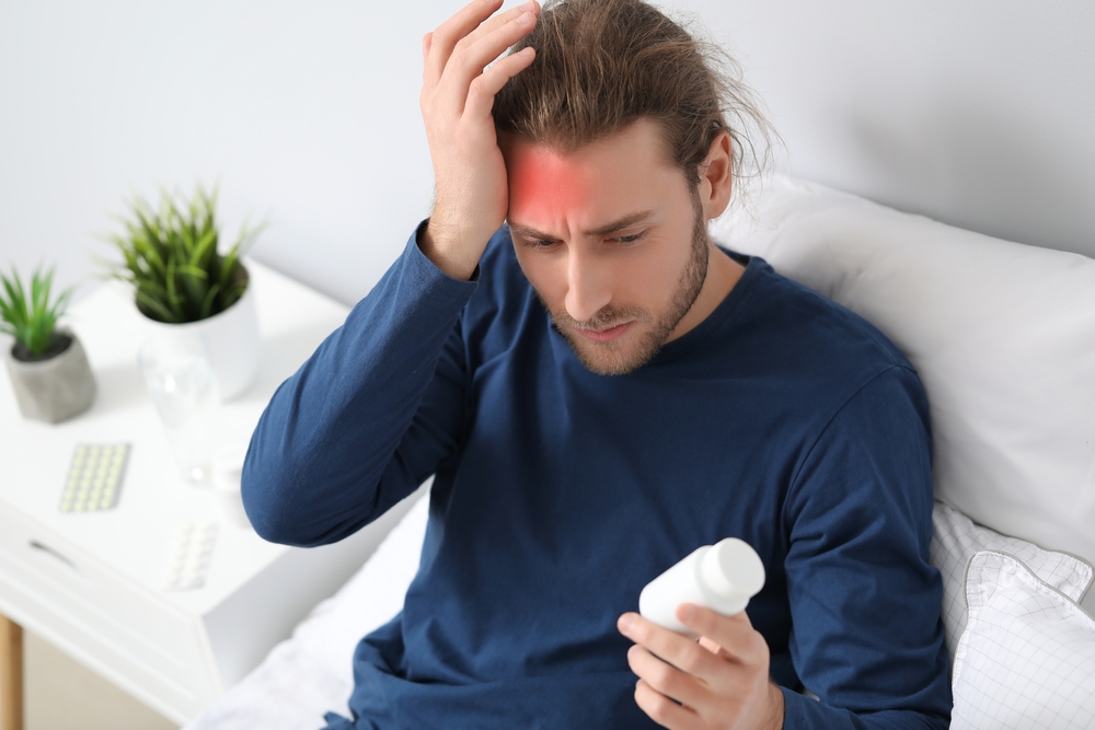 Ein Mann leidet unter Migräne. Er hält eine Dose mit Sumatriptan-Tabletten in der Hand.